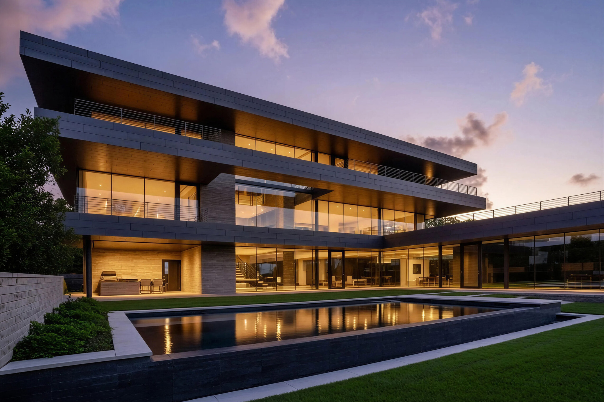 A modern, multi-story house with large glass windows and balconies, illuminated at dusk, reflected in a rectangular pool in the foreground.